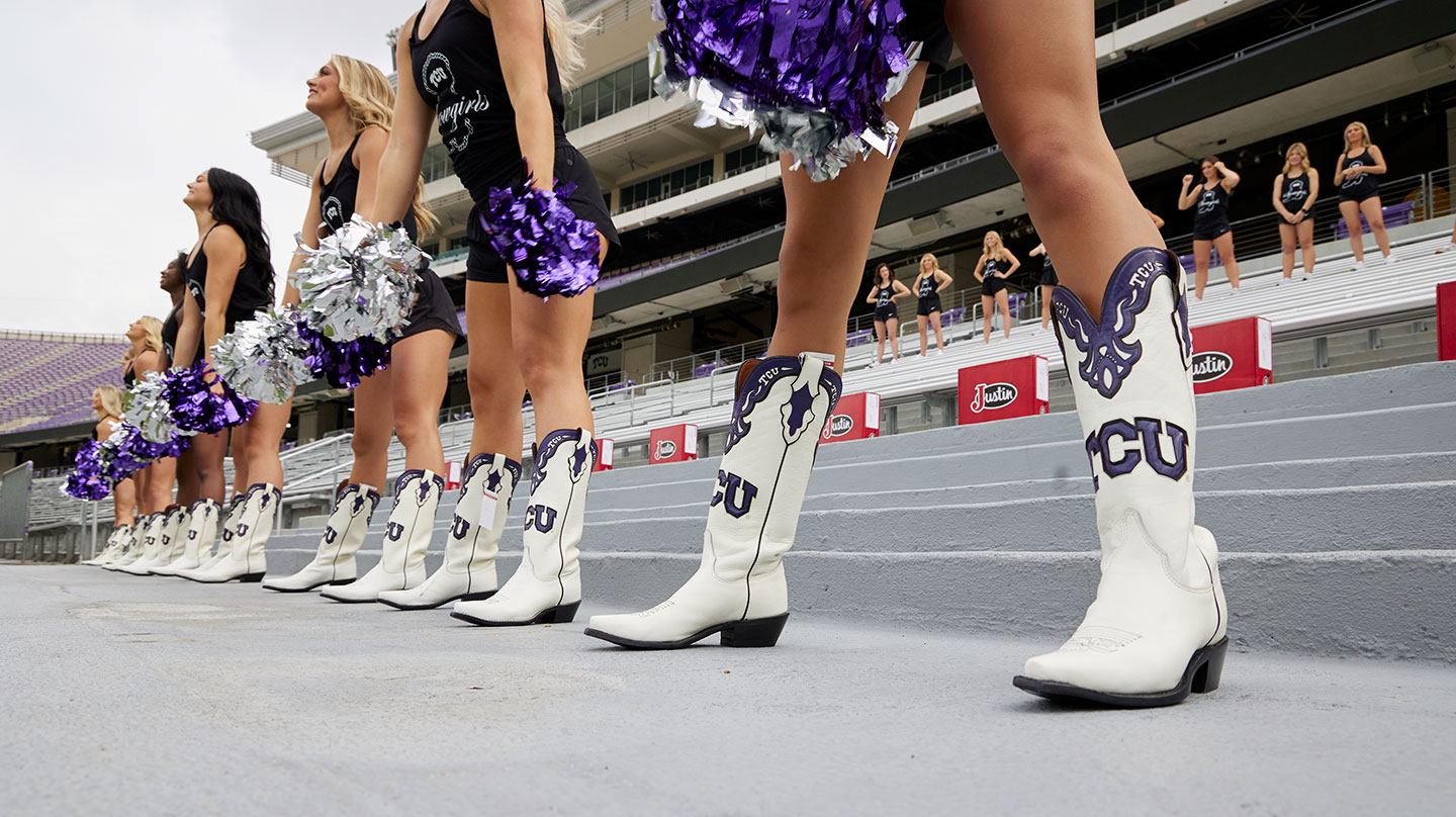 Las TCU Showgirls luciendo sus botas TCU personalizadas blancas y moradas en la práctica en las gradas del estadio.